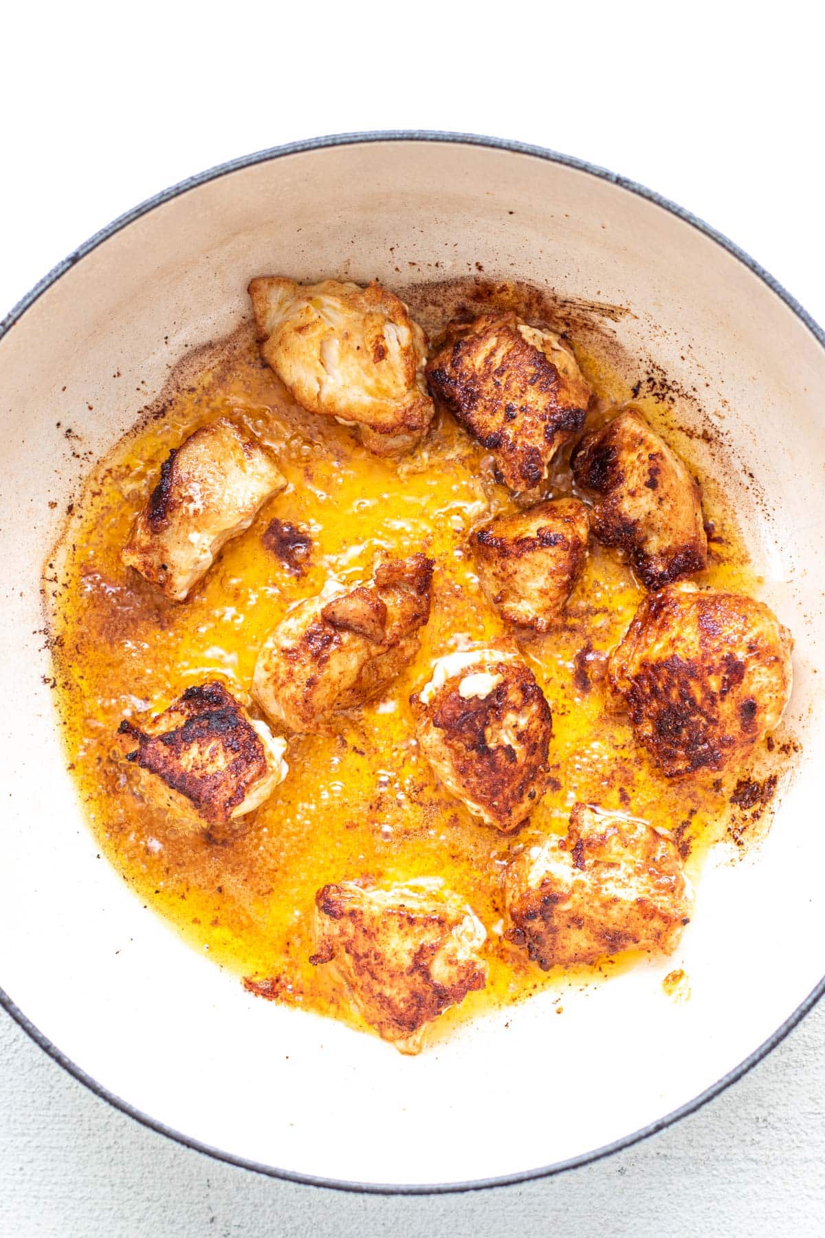 chicken breast cooking in fat inside a large white pot