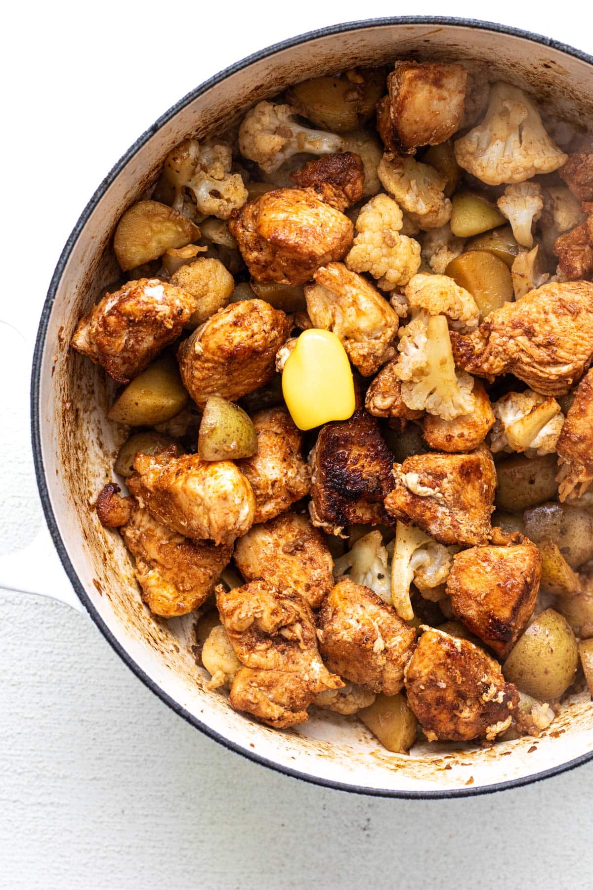 chicken and potatoes in a white pot with ghee melting on top
