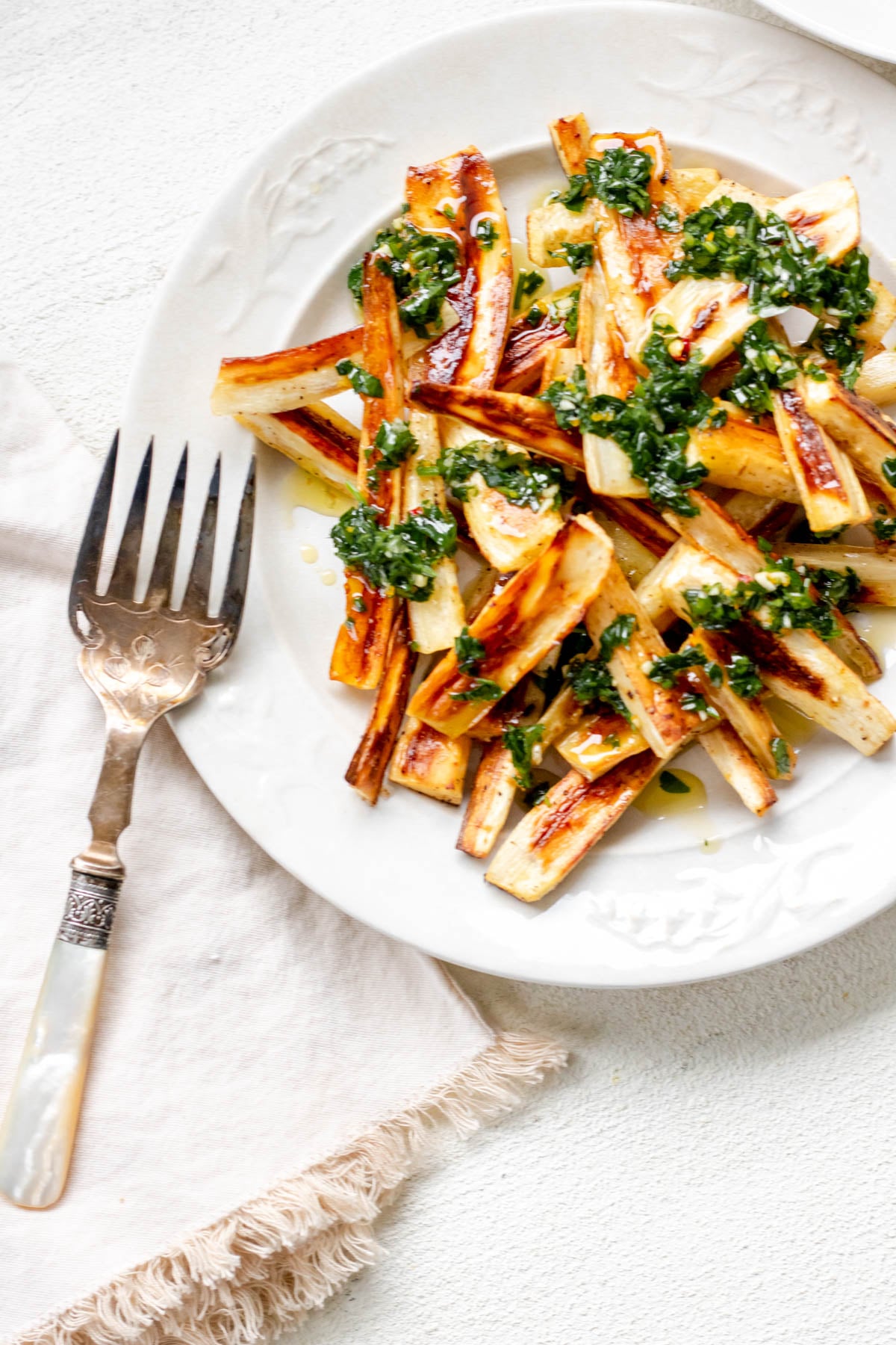 a large white plate piled high with toasty brown roasted parsnips topped with herby green chive gremolata