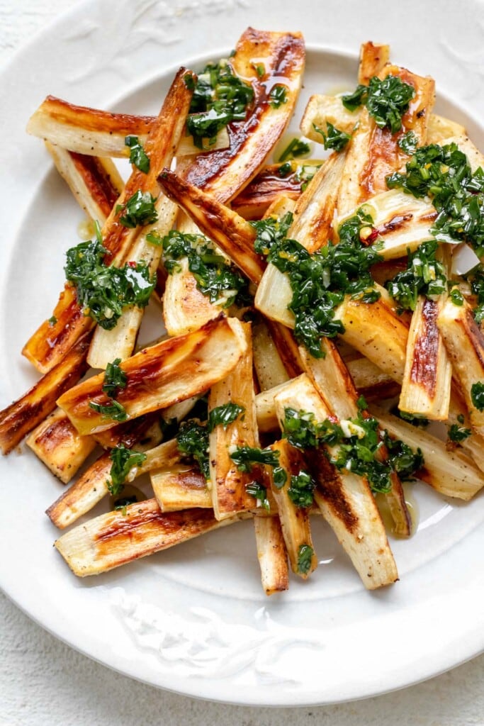 a large white plate piled high with toasty brown roasted parsnips topped with herby green chive gremolata