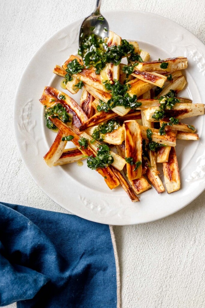 a large white plate piled high with toasty brown roasted parsnips topped with herby green chive gremolata and a napkin in the background