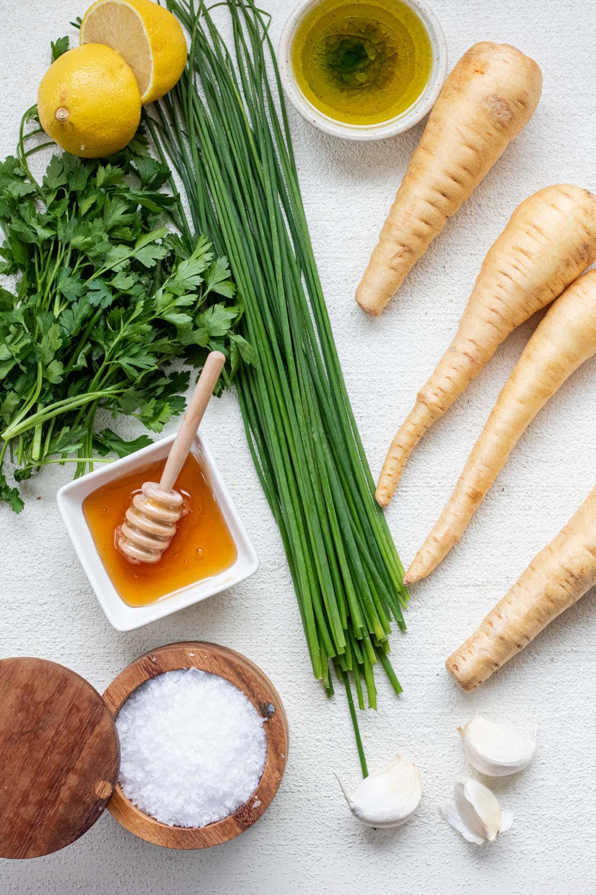 Parsnips, chives, oney, parsley, and salt all lying on a hard white surface