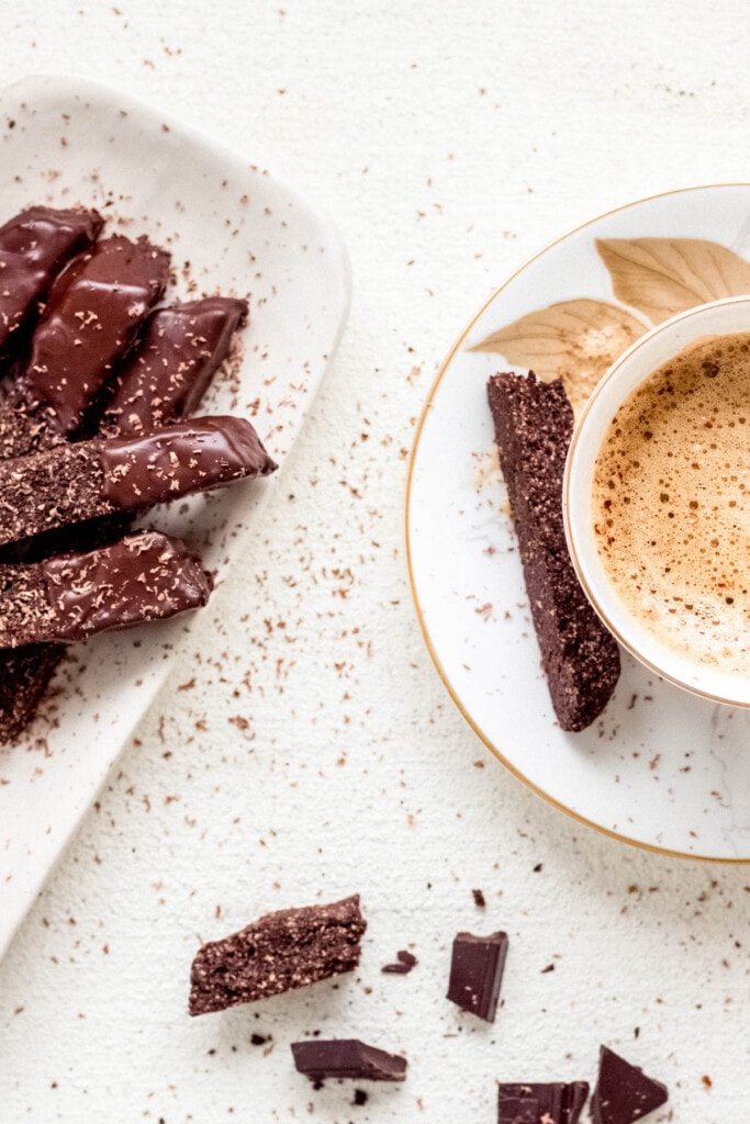 A small rectangular platter filled with coffee cardamom biscotti dipped in dark chocolate and a mug of hot coffee on the side