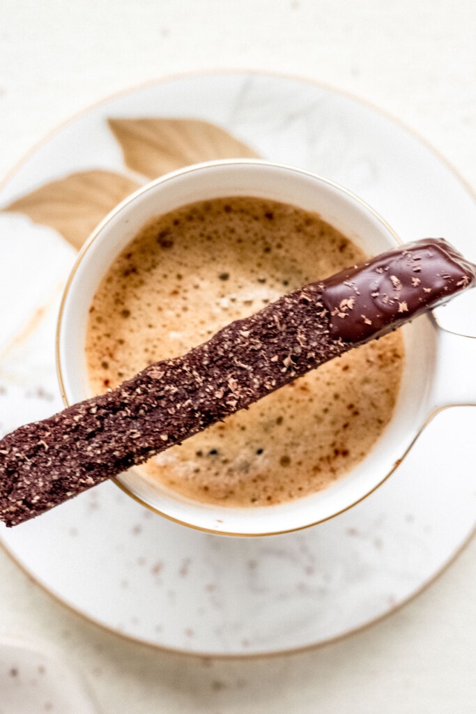 chocolate cardamom coffee gluten free biscotti dipped in dark chocolate placed on top of a mug with hot coffee