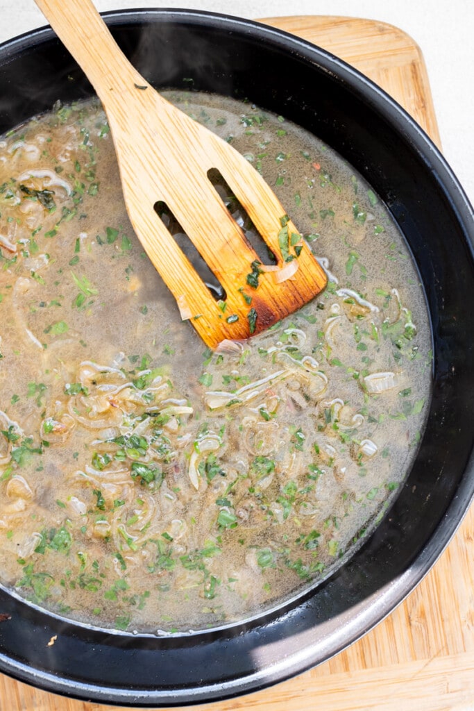 a wooden spoon stirring wine, tarragon, and shallot sauce