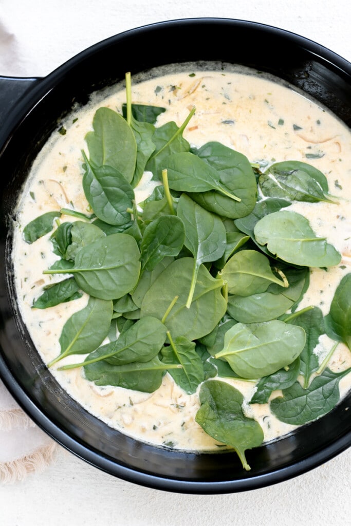 a cast iron skillet with a cream sauce and spinach wilting