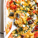 baked spaghetti squash with olives and tomatoes in a rectangular serving dish with a spoon