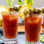 2 glasses of bloody mary garnished with olives, celery, and lemon slices.