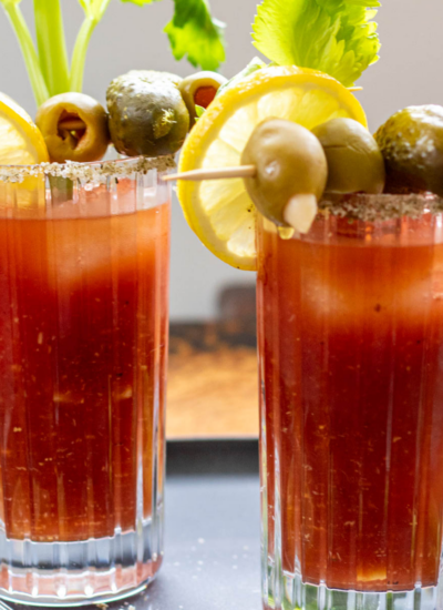 2 glasses of bloody mary garnished with olives, celery, and lemon slices.