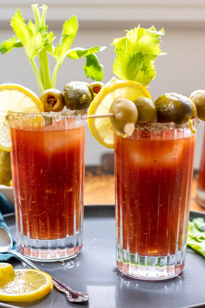 two glasses of bloody mary with pickle, olive, celery, and lemon