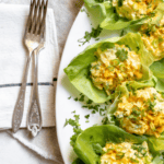 egg salad in lettuce cups on an oval platter next to two forks on a napkin
