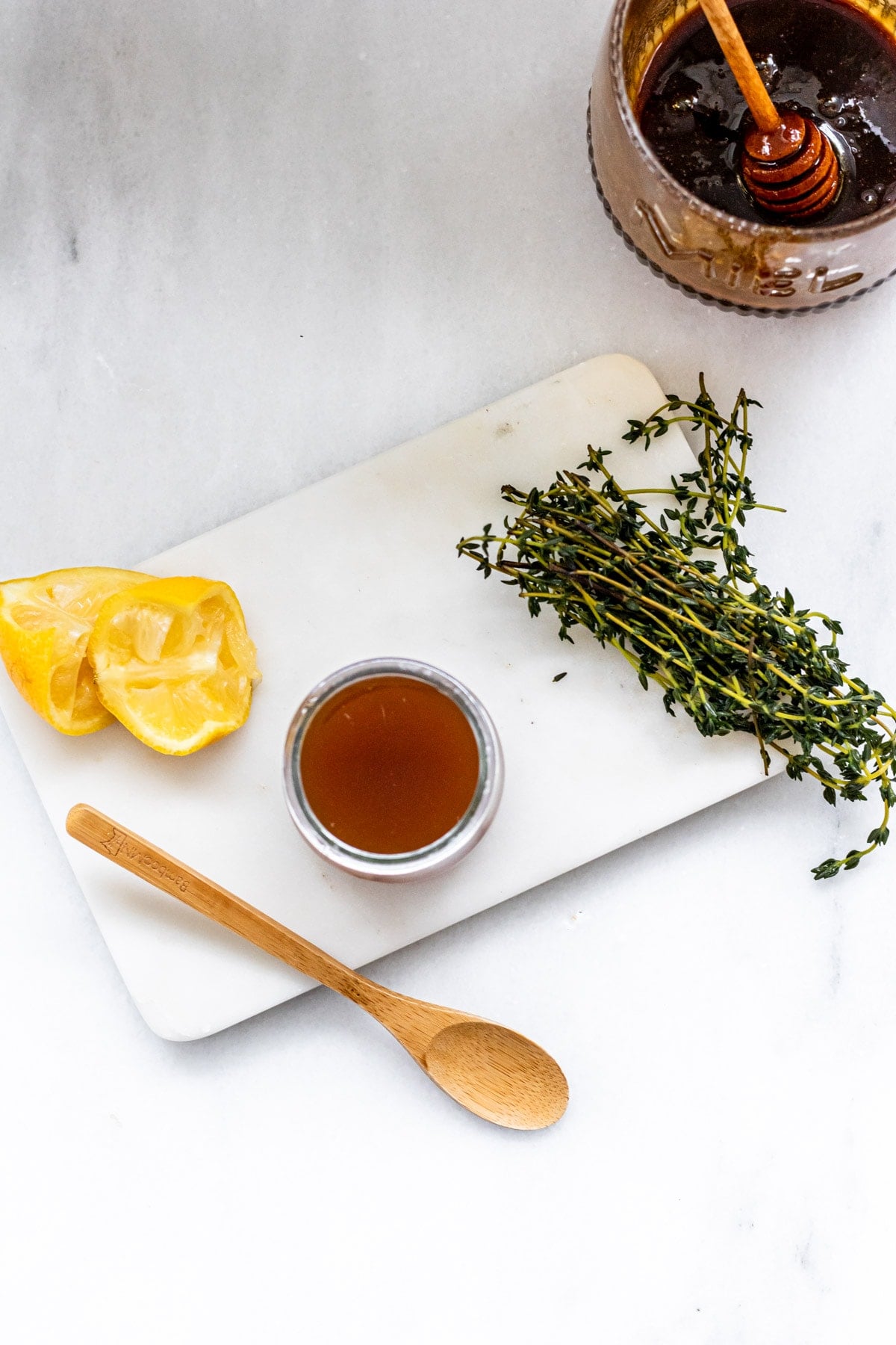 a small jar of homemade cough syrup, 2 squeezed lemons, fresh thyme, and a wooden spoon