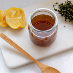 a small jar of homemade cough syrup, 2 squeezed lemons, fresh thyme, and a wooden spoon