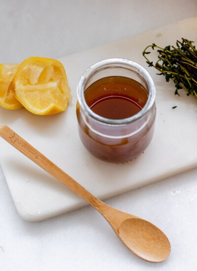 a small jar of homemade cough syrup, 2 squeezed lemons, fresh thyme, and a wooden spoon