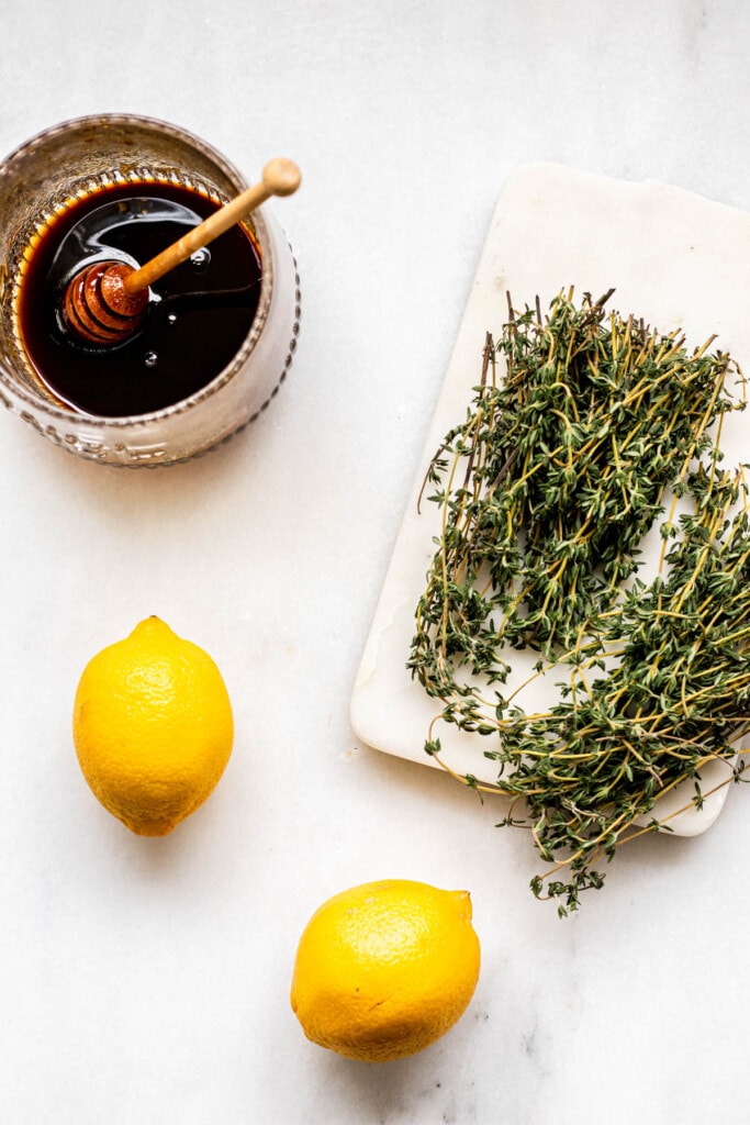 a bunch of thyme, a pot of honey, and 2 lemons on a white background