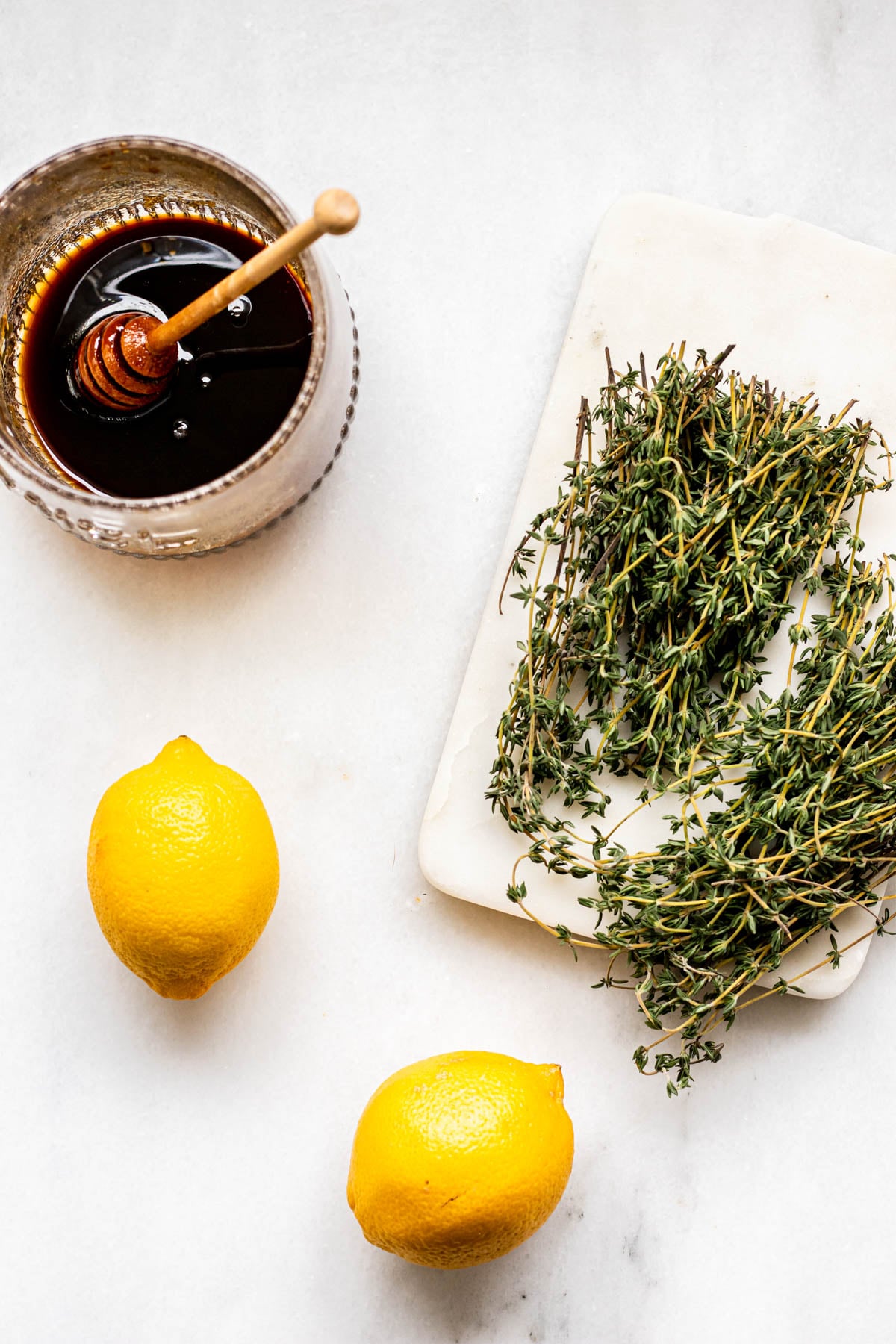 a bunch of thyme, a pot of honey, and 2 lemons on a white background