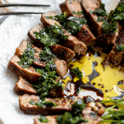 sliced steak with an herb dressing on a white plate with a fork