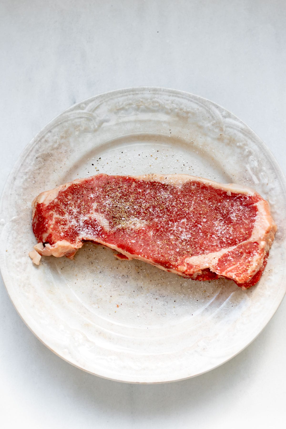 steak seasoned with salt and pepper on a plate