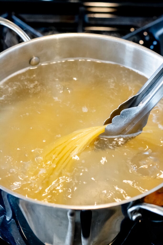 a pot of pasta cooking in boiling water with tongs holding the al dente pasta