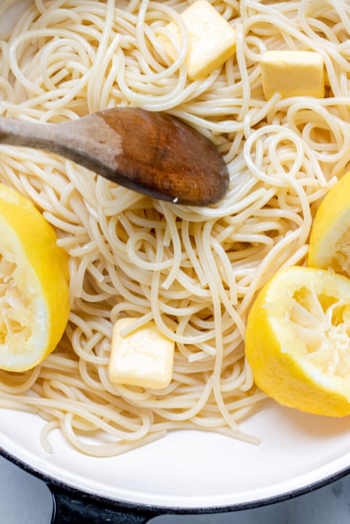 a pot of pasta with lemon and butter and a wooden spoon