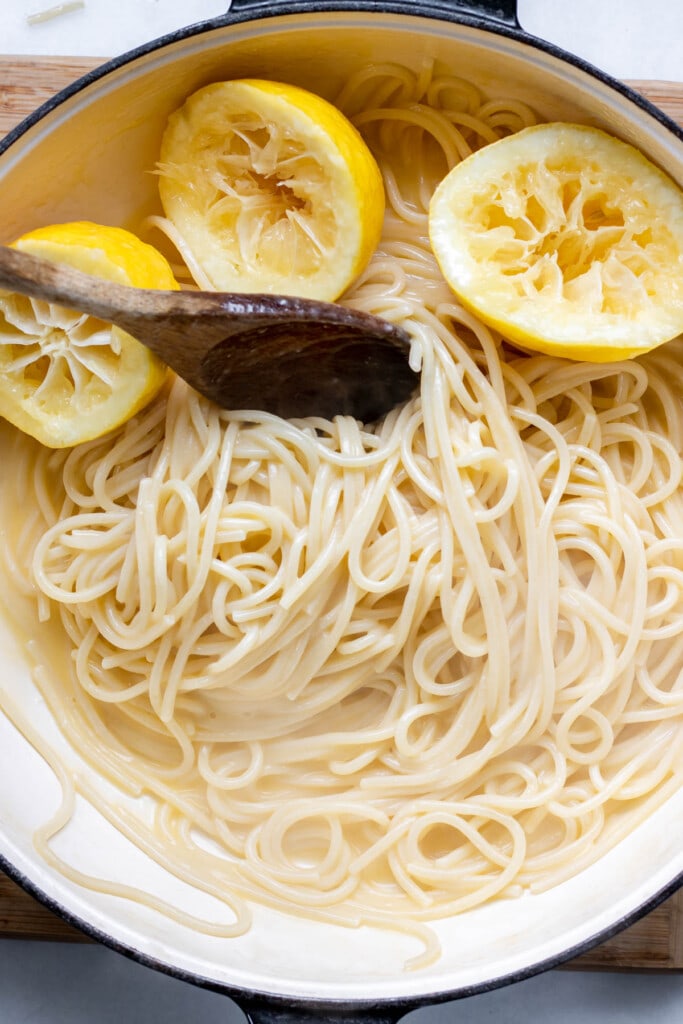 a pot of pasta with lemon pieces and tongs stirring the pasta