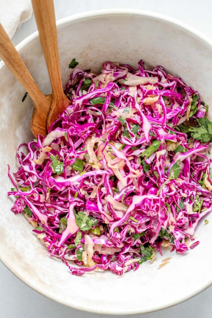 Bowl of cabbage probiotic sauerkraut slaw with serving utensils.