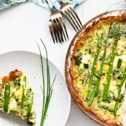 plate with asparagus quiche slice and pie plate of asparagus quiche next to it with forks in the background