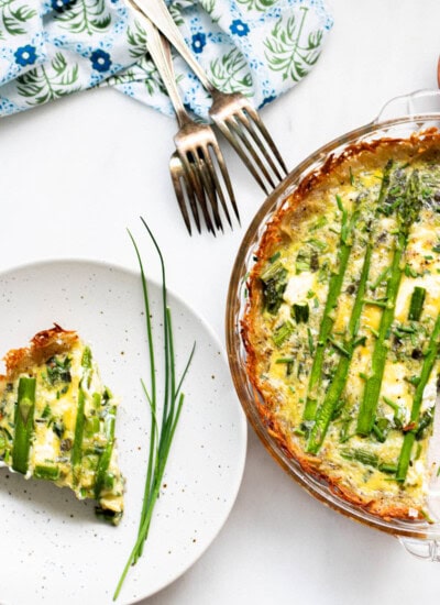 plate with asparagus quiche slice and pie plate of asparagus quiche next to it with forks in the background