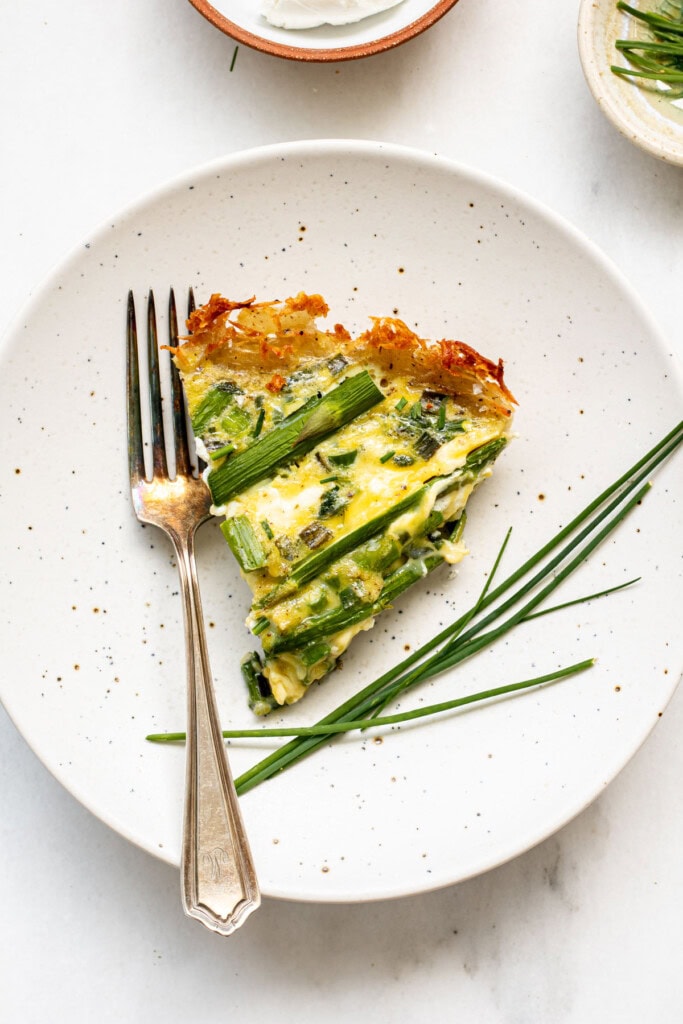 white plate with asparagus quiche and a fork on plate