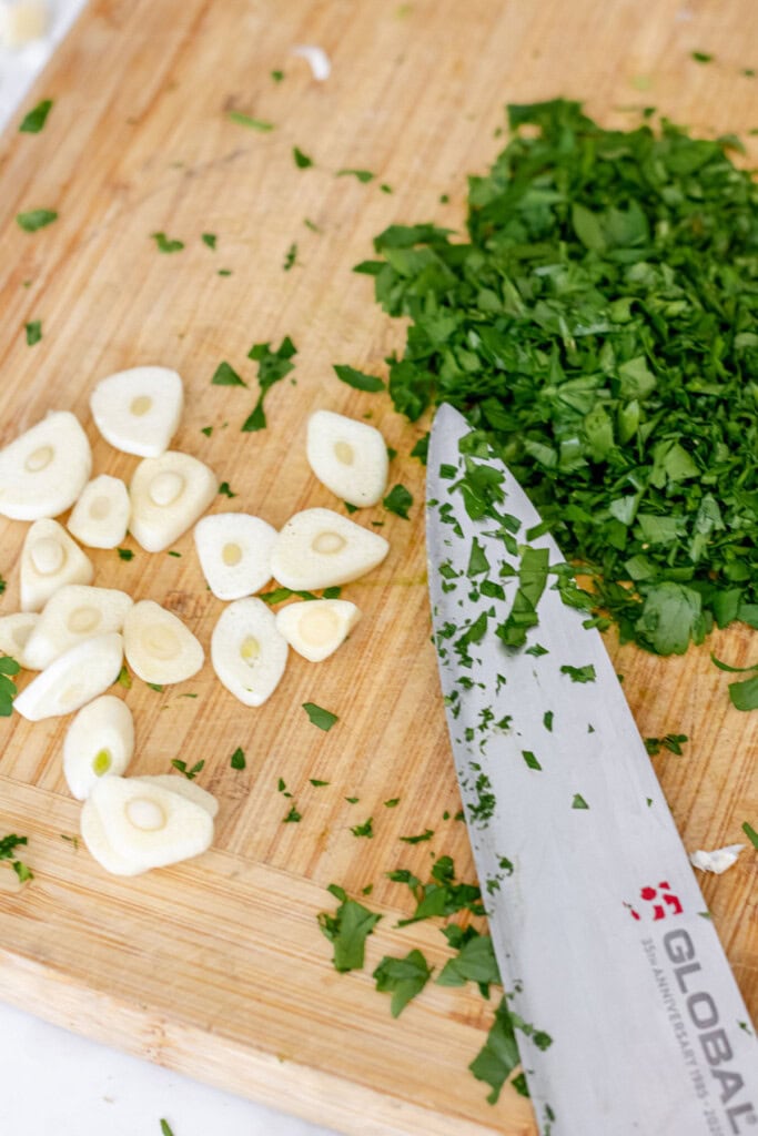 knife on cutting board cutting garlic and parsley