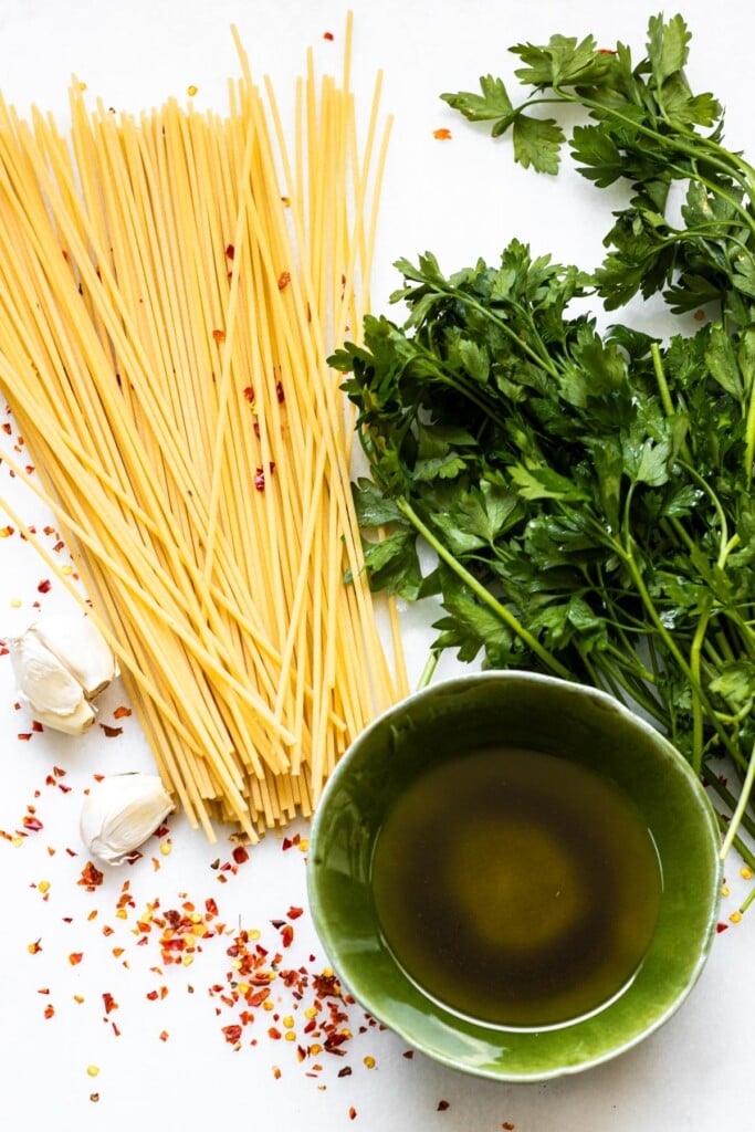 raw ingredients on white background, spaghetti, garlic, oil, parsley, and crushed red pepper