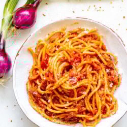 bowl of bucatini all'amatraciana with red onion in the background