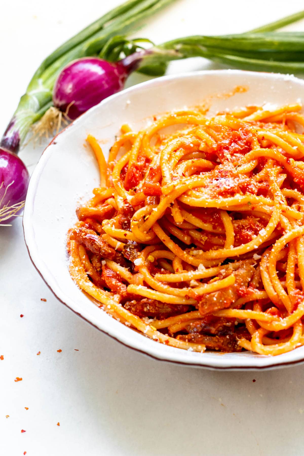 bowl of bucatini all'amatraciana with red onion in the background