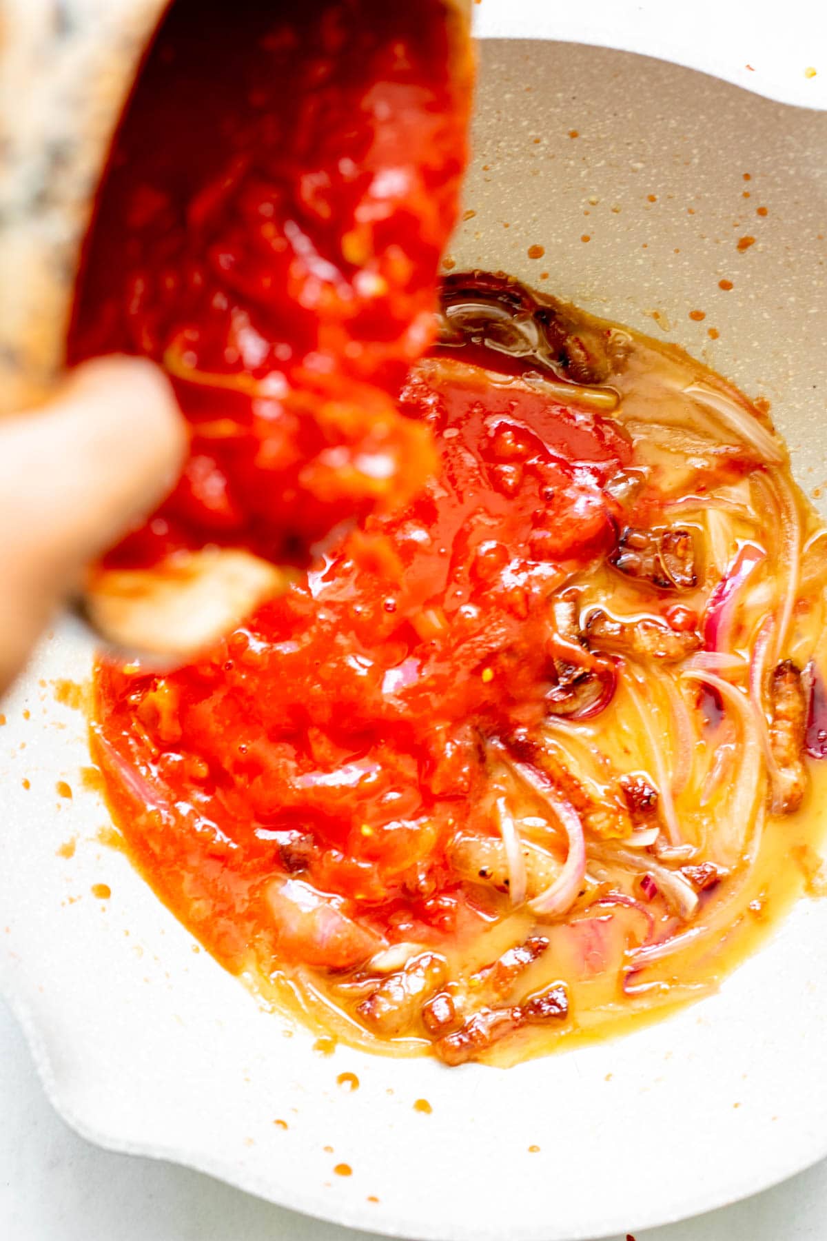 pouring tomato into sauteed red onion and guaciale