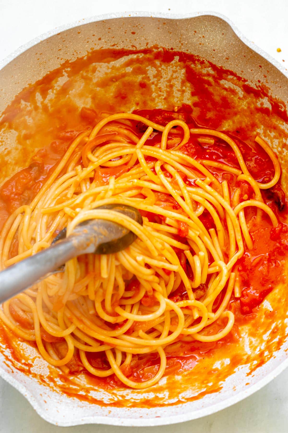 tongs tossing pasta in tomato sauce