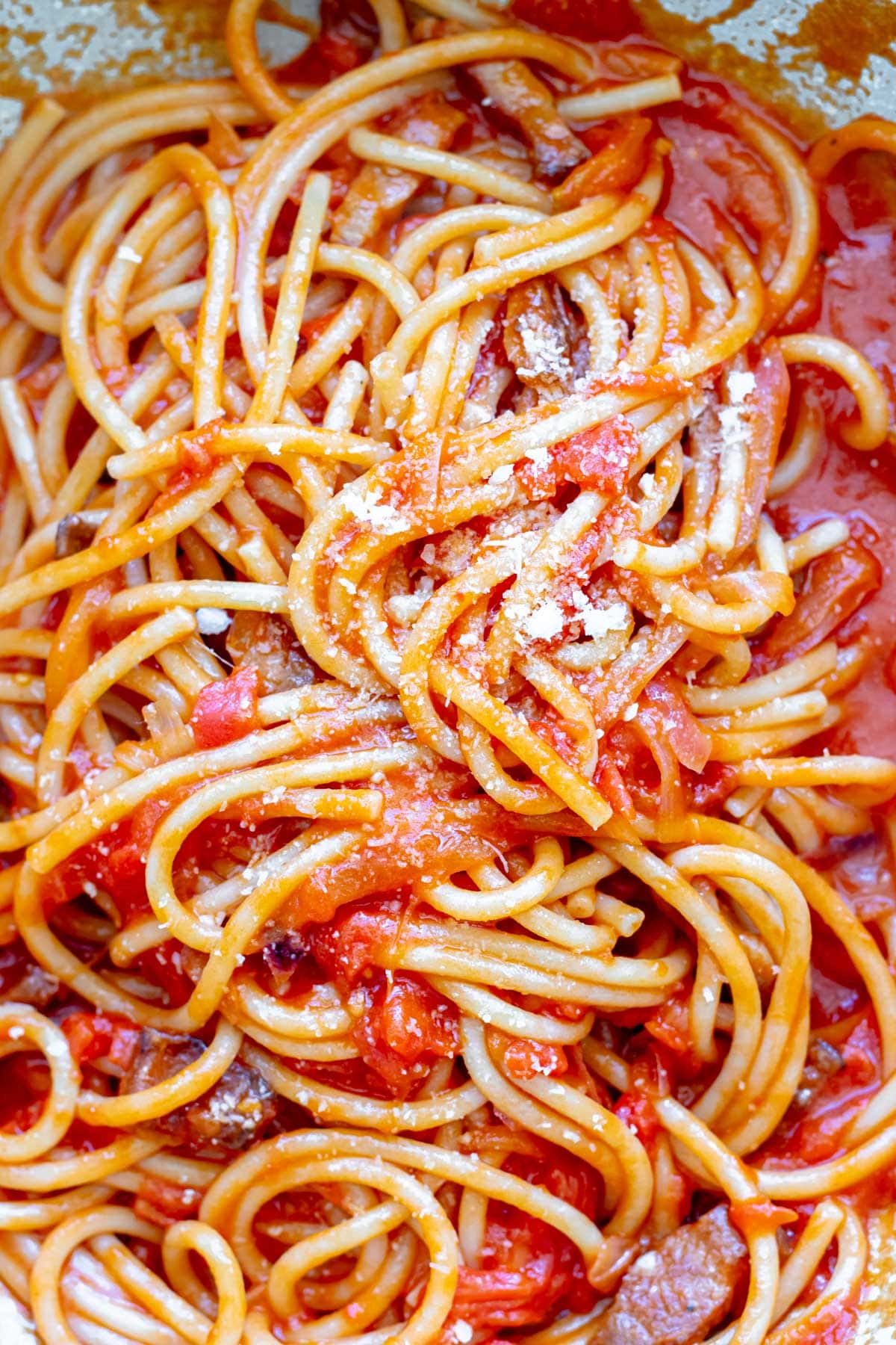 large pan of bucatini tossed in tomato sauce for bucatini all'amatraciana