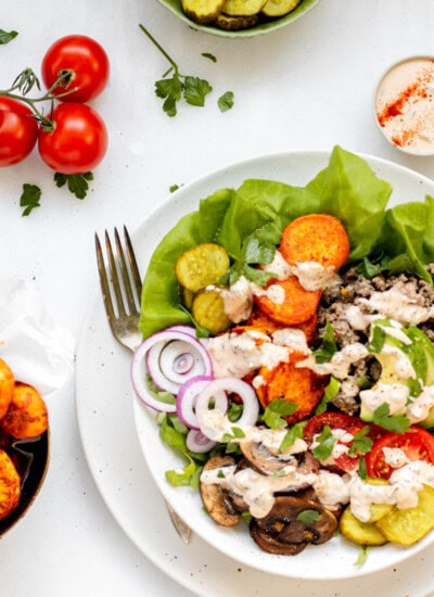 Healthy burger bowl with fork resting on the bowl and tomatoes and special sauce on the side