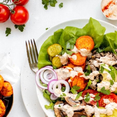 Healthy burger bowl with fork resting on the bowl and tomatoes and special sauce on the side