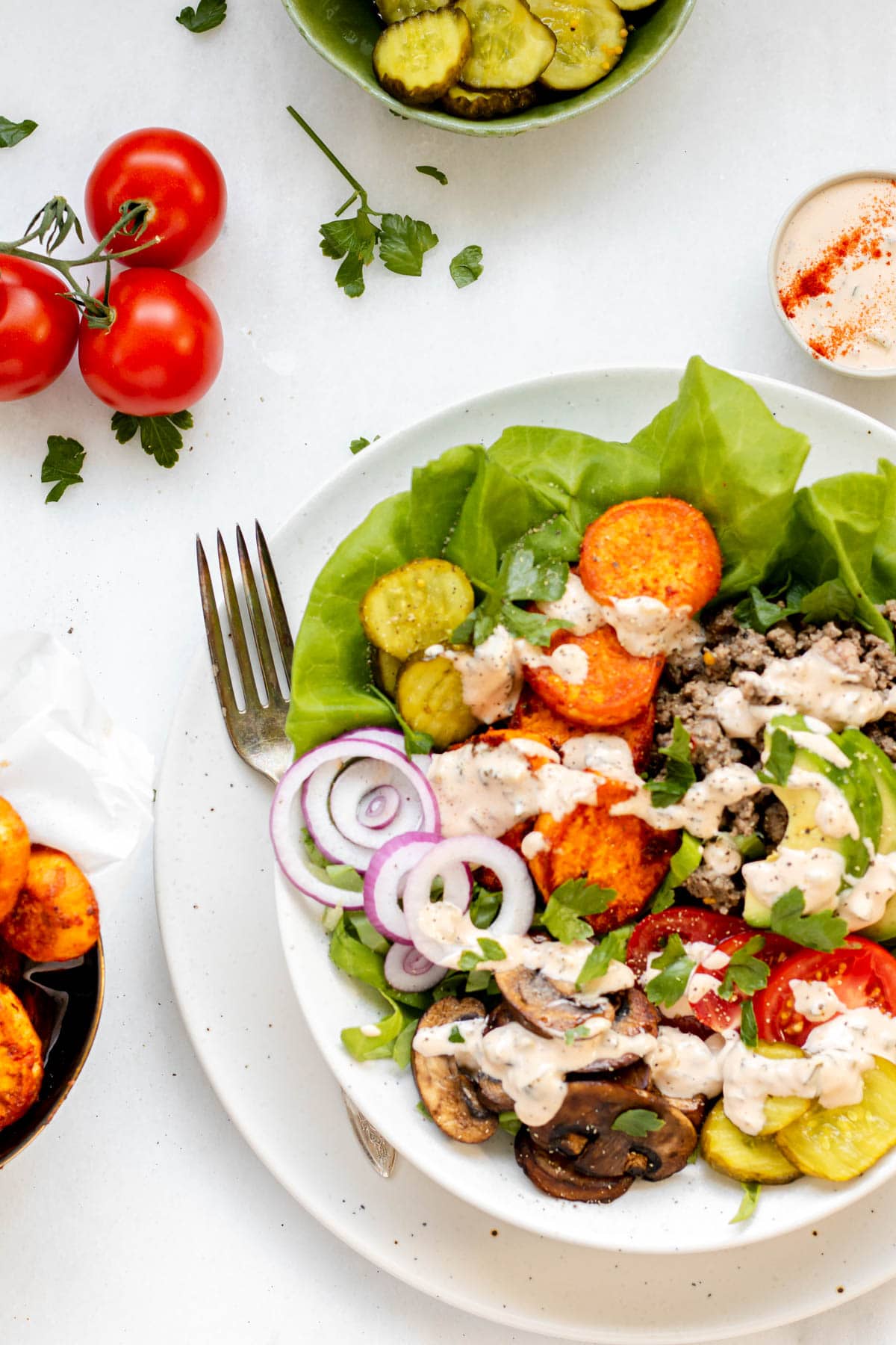 Healthy burger bowl with fork resting on the bowl and tomatoes and special sauce on the side