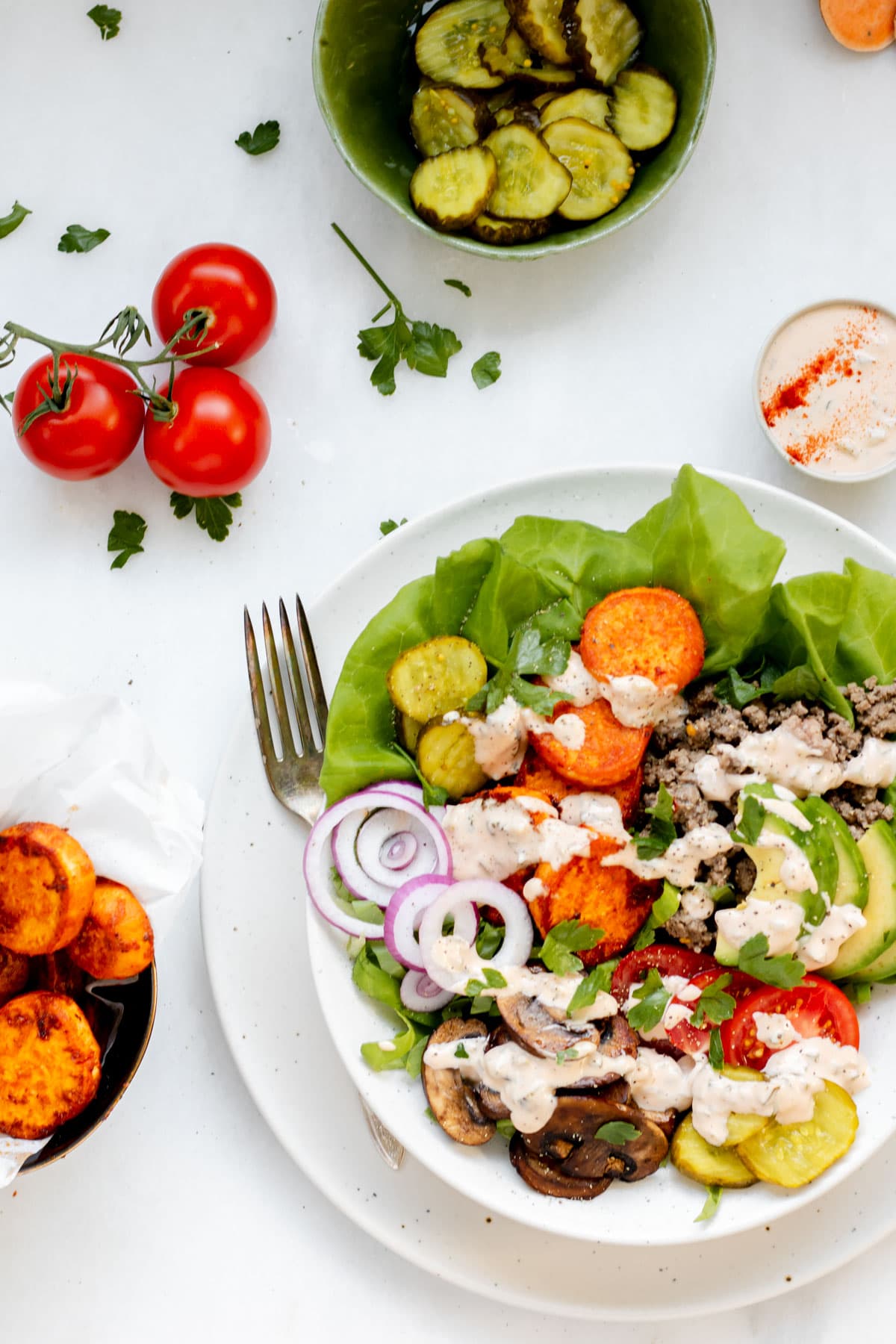 Healthy burger bowl with fork resting on the bowl and tomatoes and special sauce on the side
