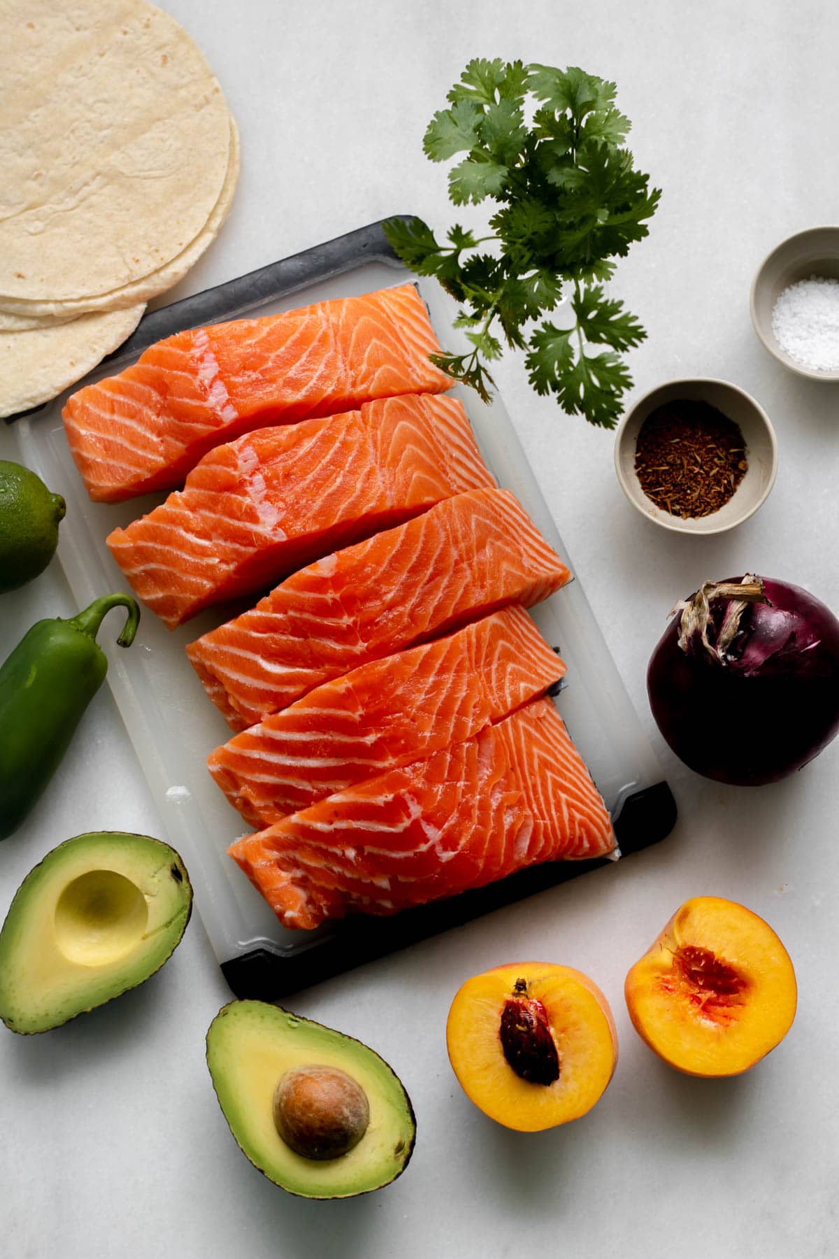 Ingredients on a white background for salmon tacos including salmon, peaches, avocado and jalapeno