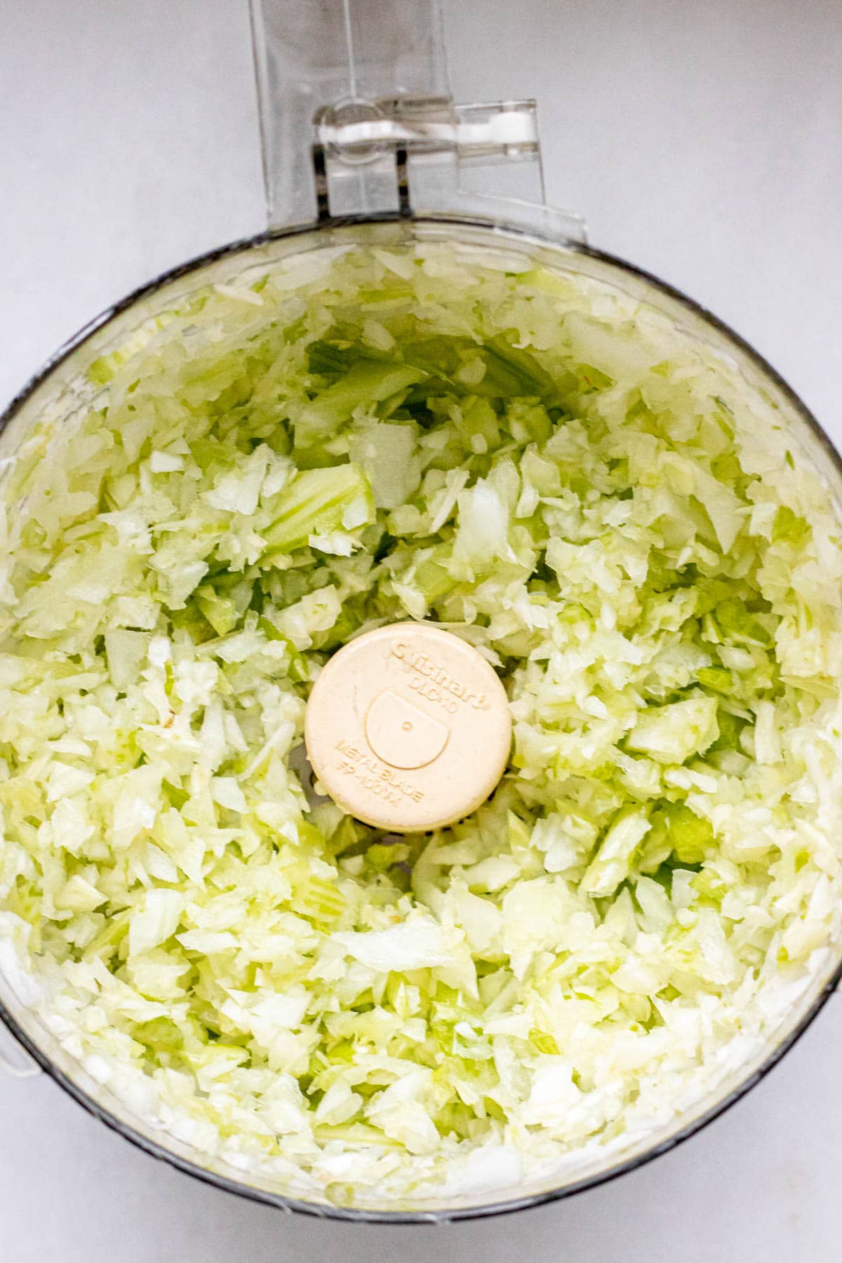 food processor bowl filled with chopped celery, fennel, and onion