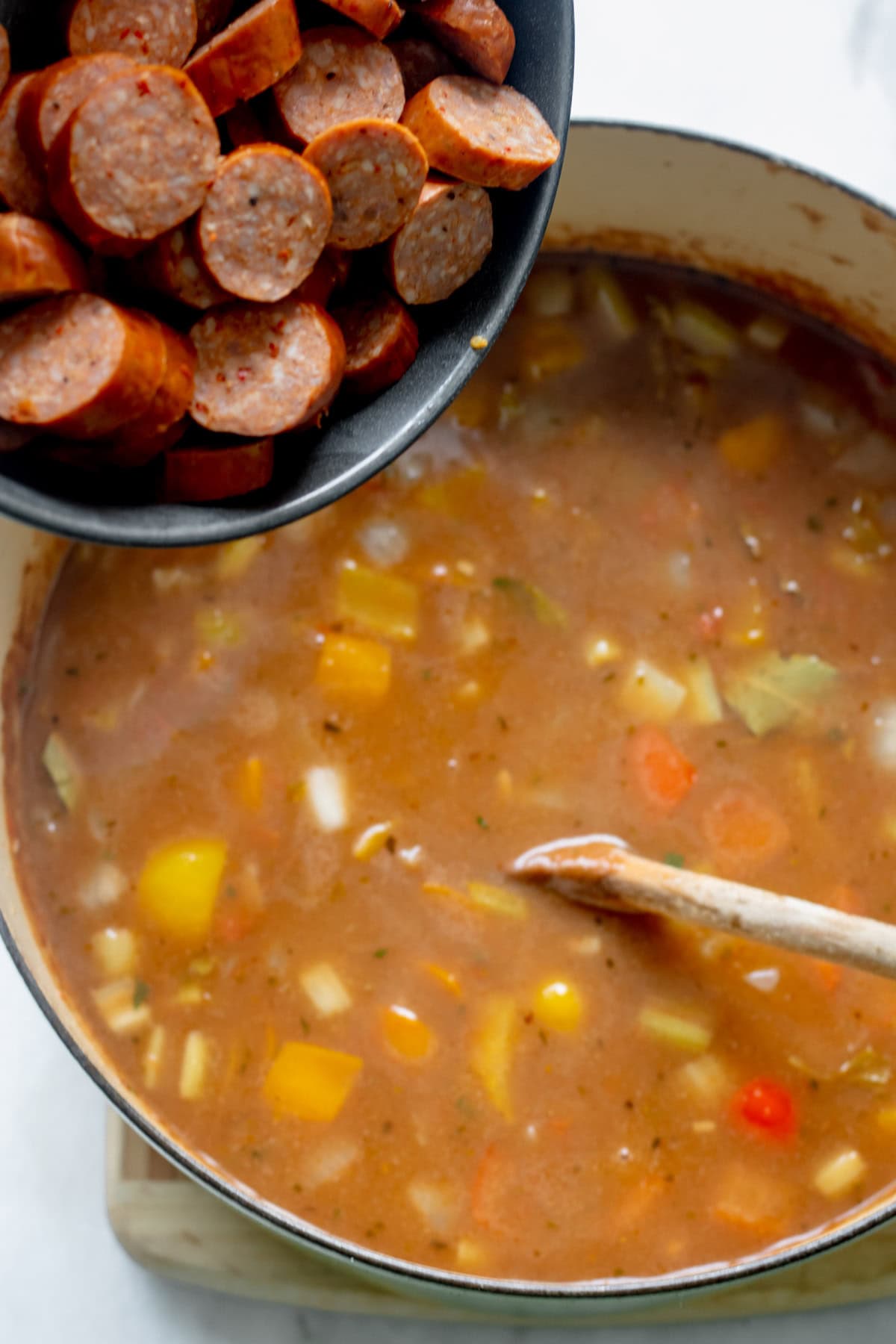 adding andouille sausage to a pot of gumbo