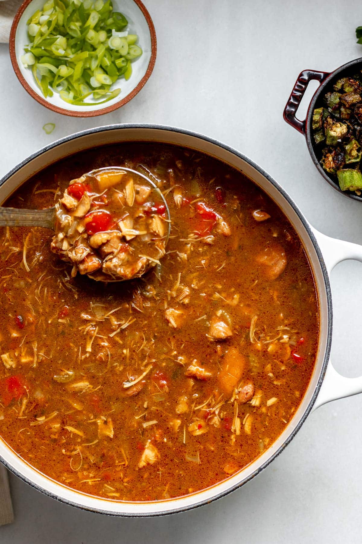 pot of gluten free chicken and sausage gumbo with okra in a small bowl in the background