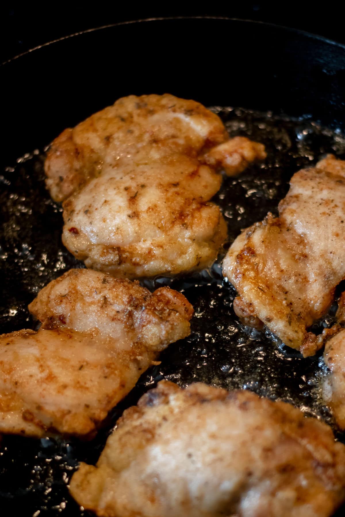 chicken thighs sizzling in a pan