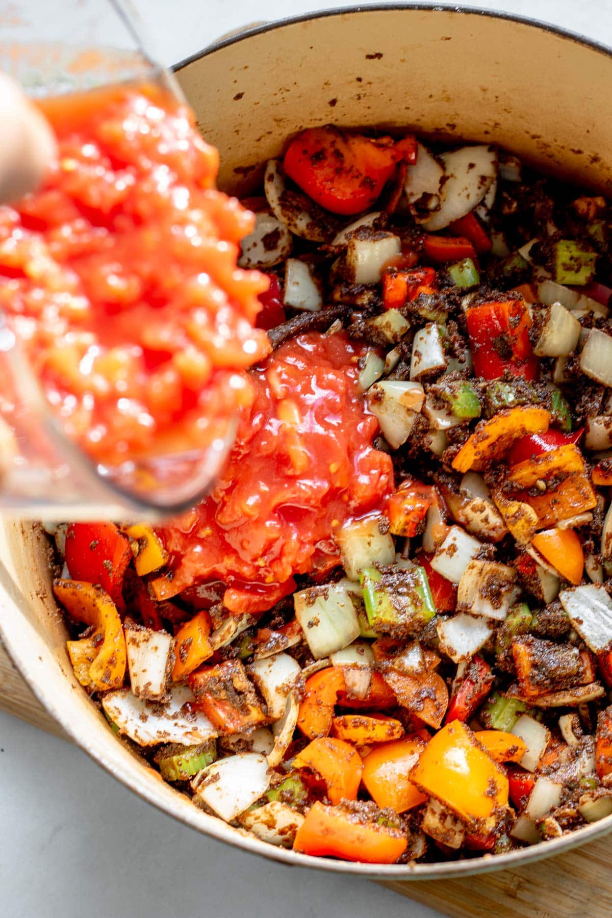 adding tomatoes to a pot of gumbo
