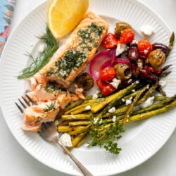 a white plate with greek salmon, asparagus, olives, and tomatoes