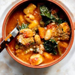 a close up photo of a spoon inside a bowl of minestrone soup with meatballs
