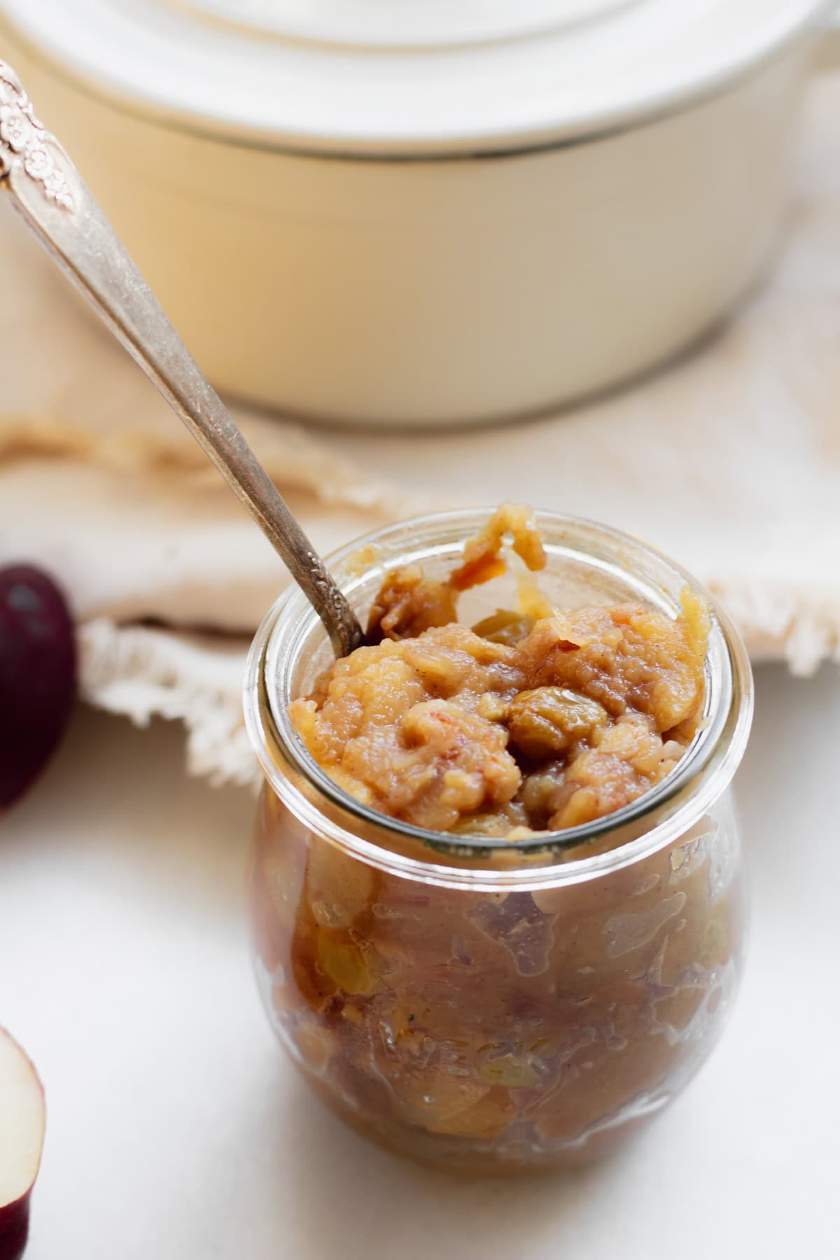 small jar of cooked apple chutney with an apple and a pot in the background