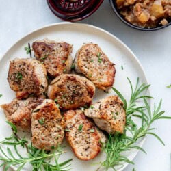 juicy pork medallions on a plate with fresh rosemary and apple chutney in the background